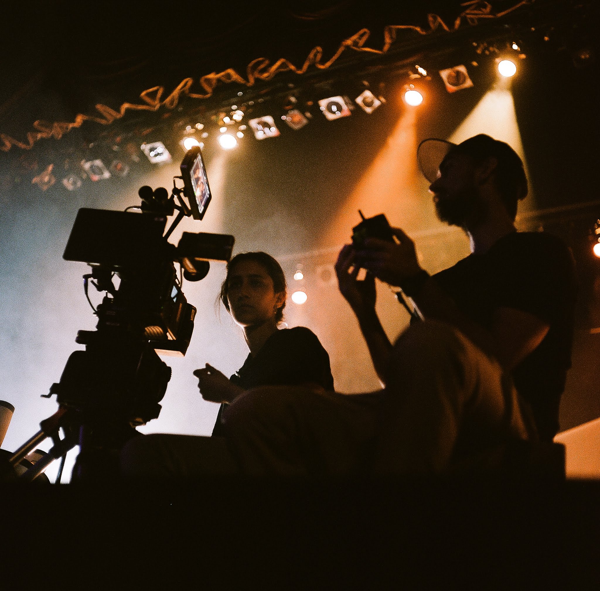 Camera and crew silhouettes under stage lights